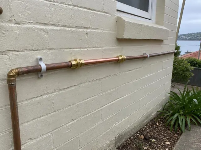 Repaired copper water pipe along an exterior brick wall near a window in Dover Heights